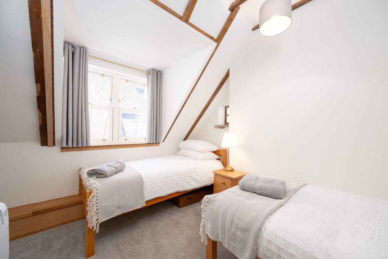 Cozy twin bedroom with white linens and sloped ceiling featuring wooden beams.