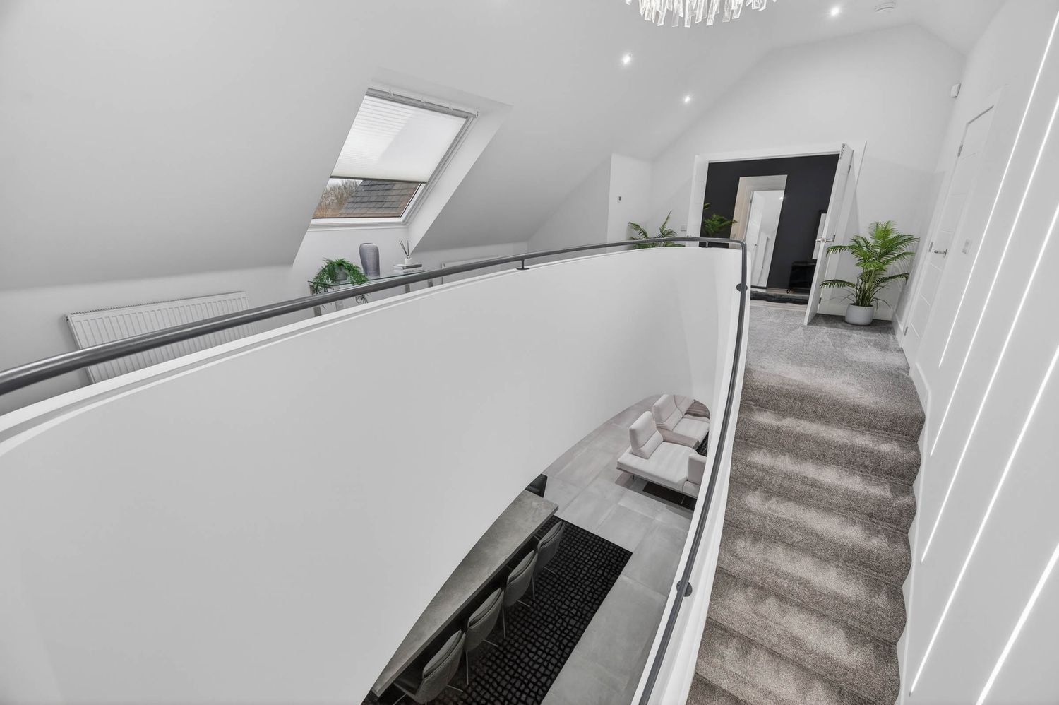 Modern white staircase with grey carpeted steps leads up to a skylight in a minimalist interior hallway.