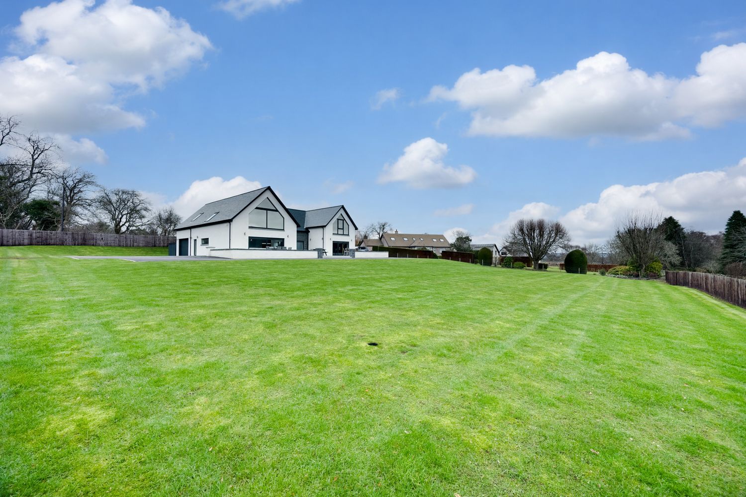 A series of lush green rolling hills and meadows with scattered buildings and blue sky with white puffy clouds.