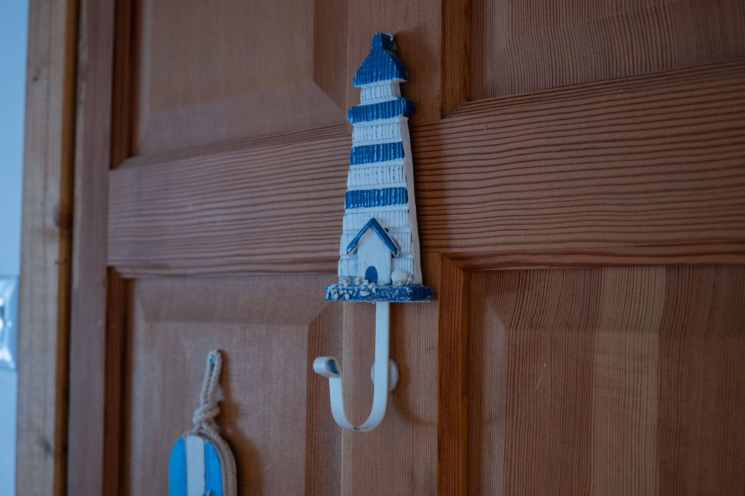 A decorative blue and white striped lighthouse wall hook mounted on a wooden door.