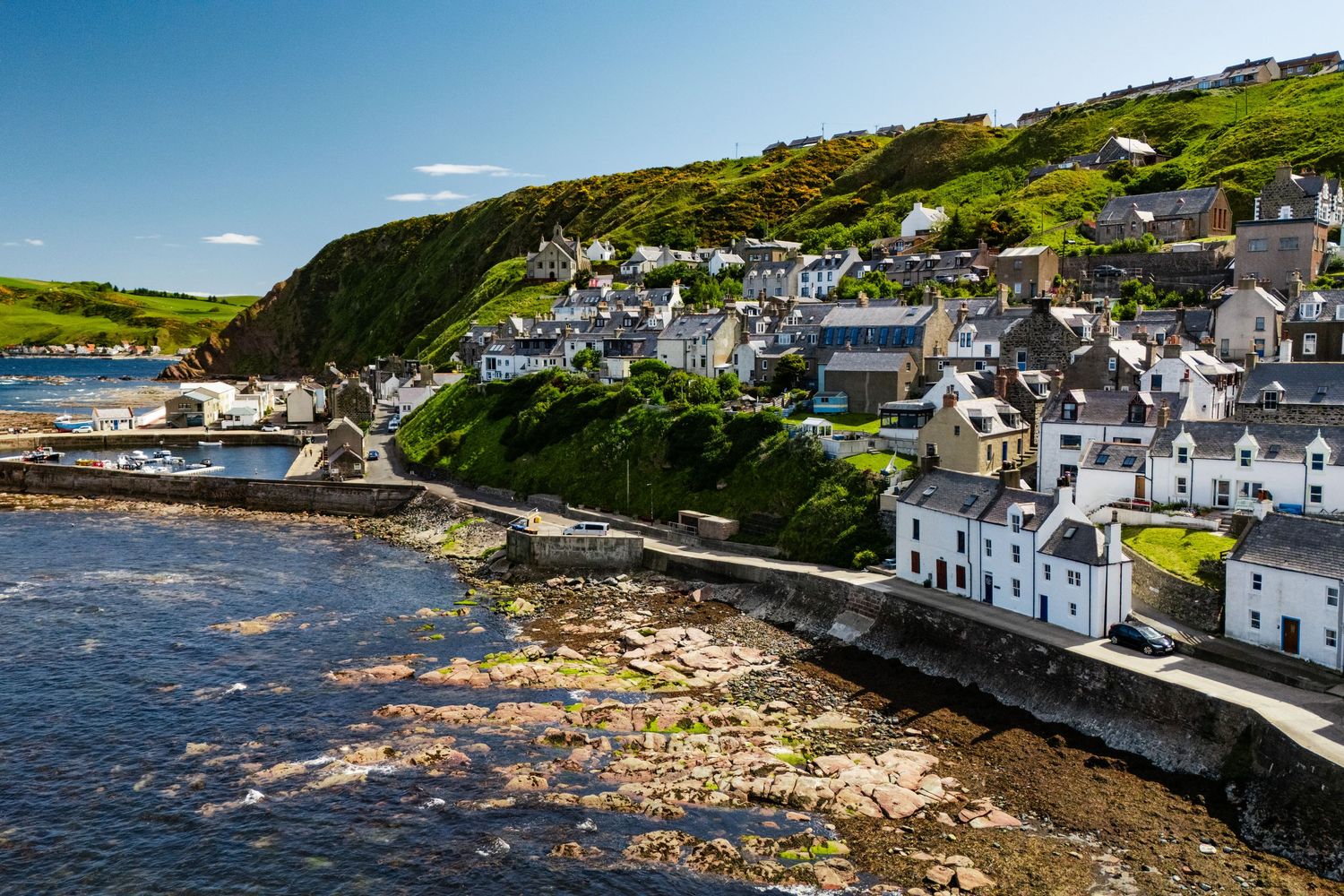 Charming coastal village with white houses nestled on hillside overlooking rocky shoreline.