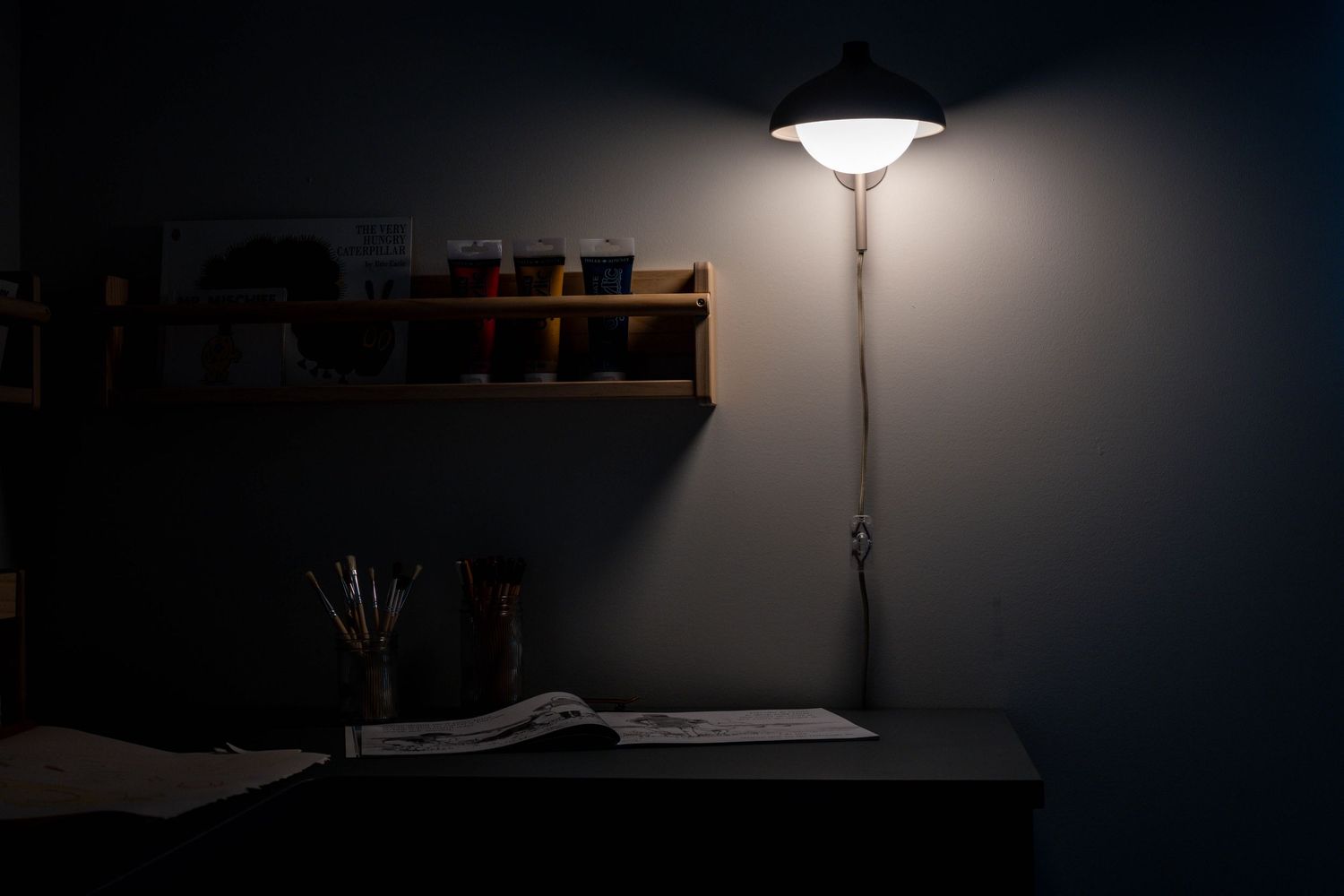 Moody desk setup with vintage floor lamp illuminating dark workspace and wooden shelving.