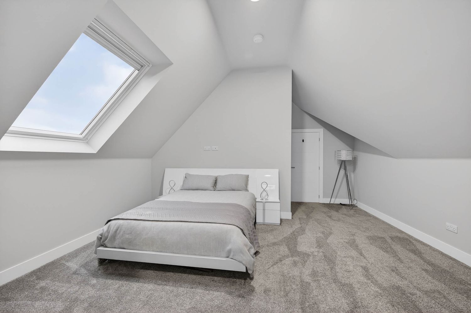 Modern attic bedroom with white walls, sloped ceiling, skylight window, and light gray wood-style flooring.