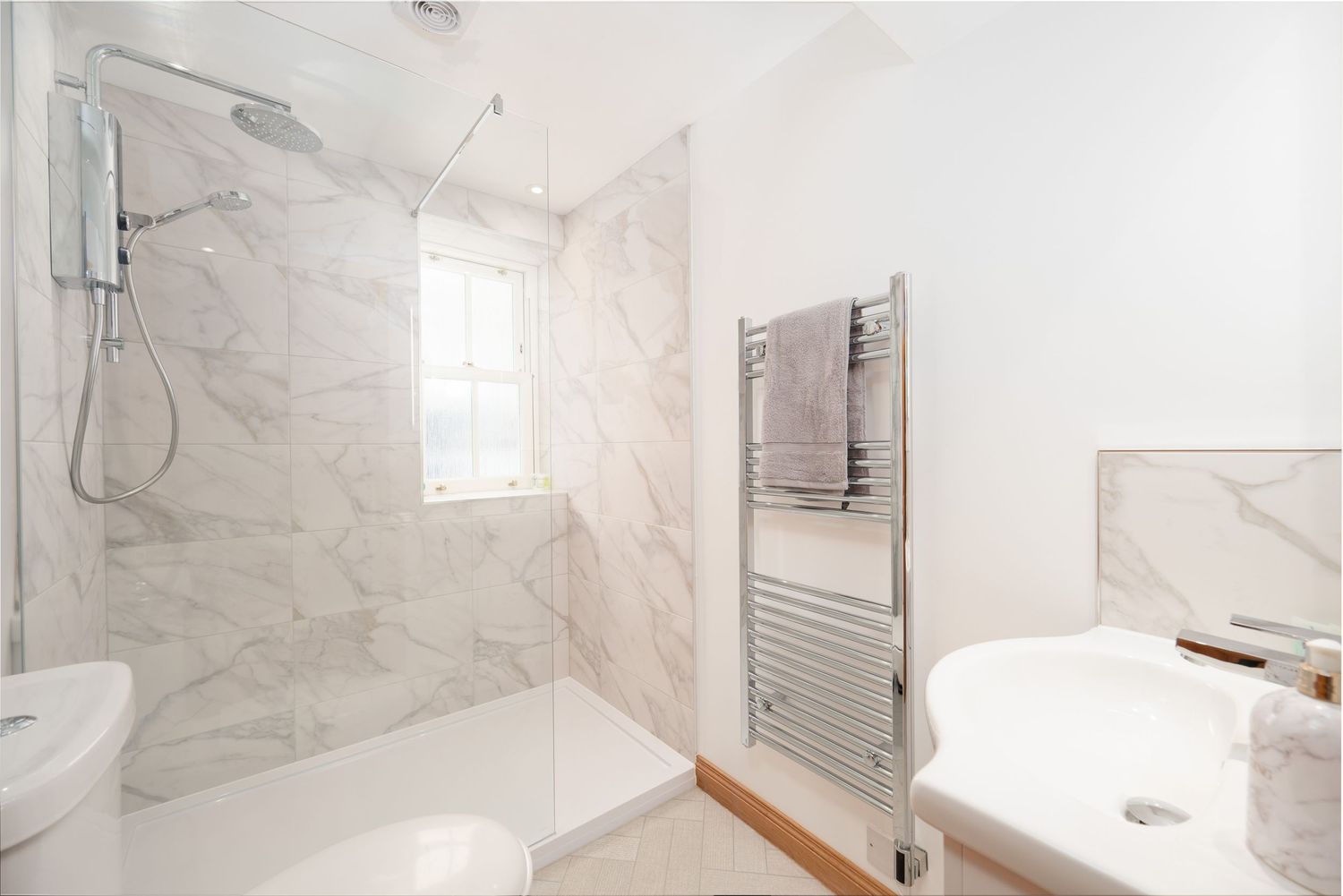 Contemporary marble-tiled bathroom with glass shower enclosure, heated towel rail, and natural light.