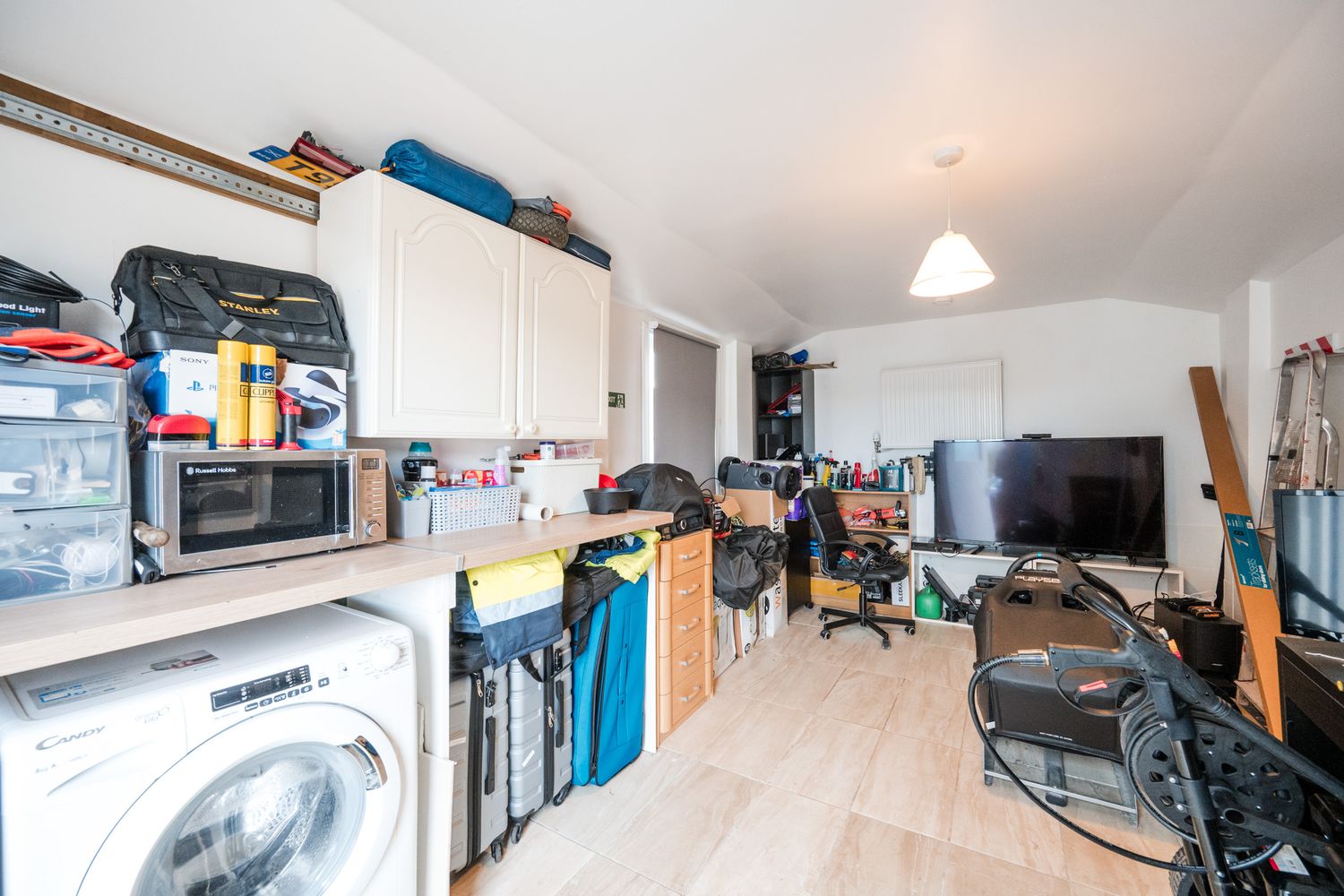 A cluttered home office space with laundry appliances, storage cabinets, and electronics against white walls.