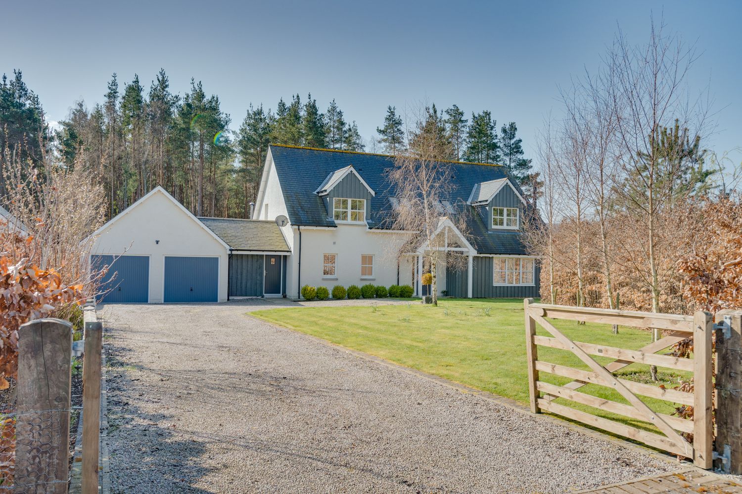 Modern country home with gray siding, double garage and wooden gate entrance on gravel driveway.