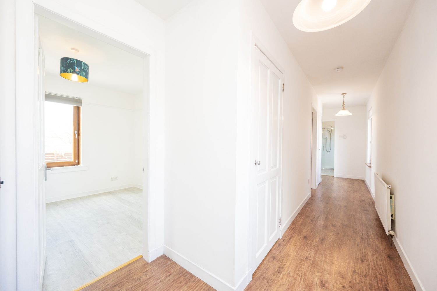 Interior hallway with wood flooring, white walls, built-in storage, and natural light from a small window.