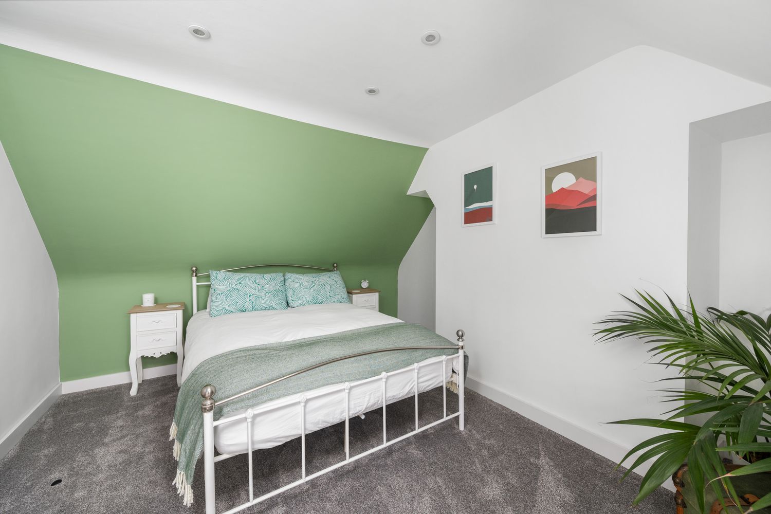 Contemporary attic bedroom featuring white metal bed frame, sage green accent wall and potted plant.