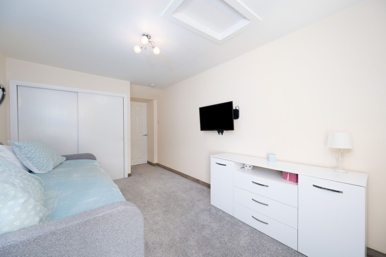 Minimalist bedroom with white furniture, wall-mounted TV, and gray carpet showcasing clean contemporary design.