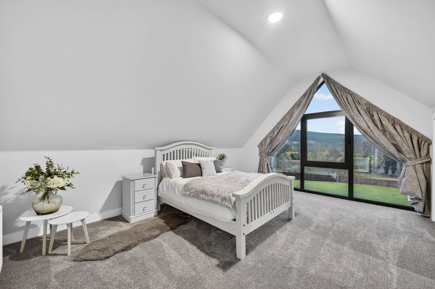 Bright white modern loft bedroom with angled ceilings features a skylight window and minimalist furnishings.
