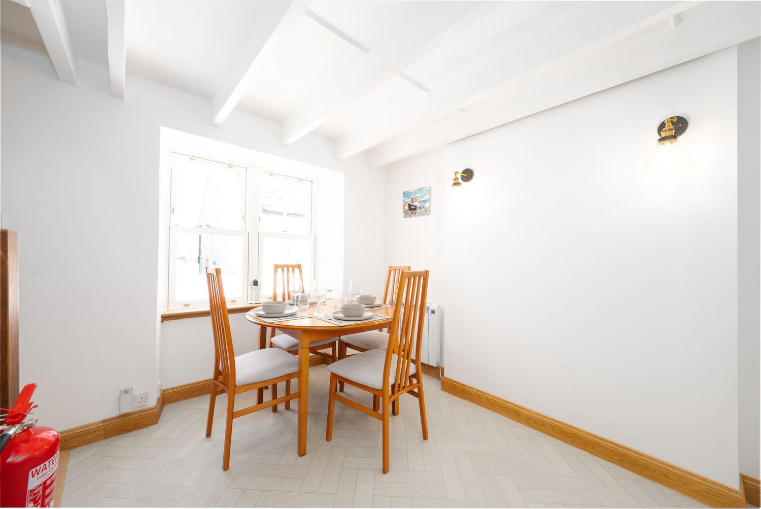 Clean white dining room with wooden table and chairs under ceiling spotlights.