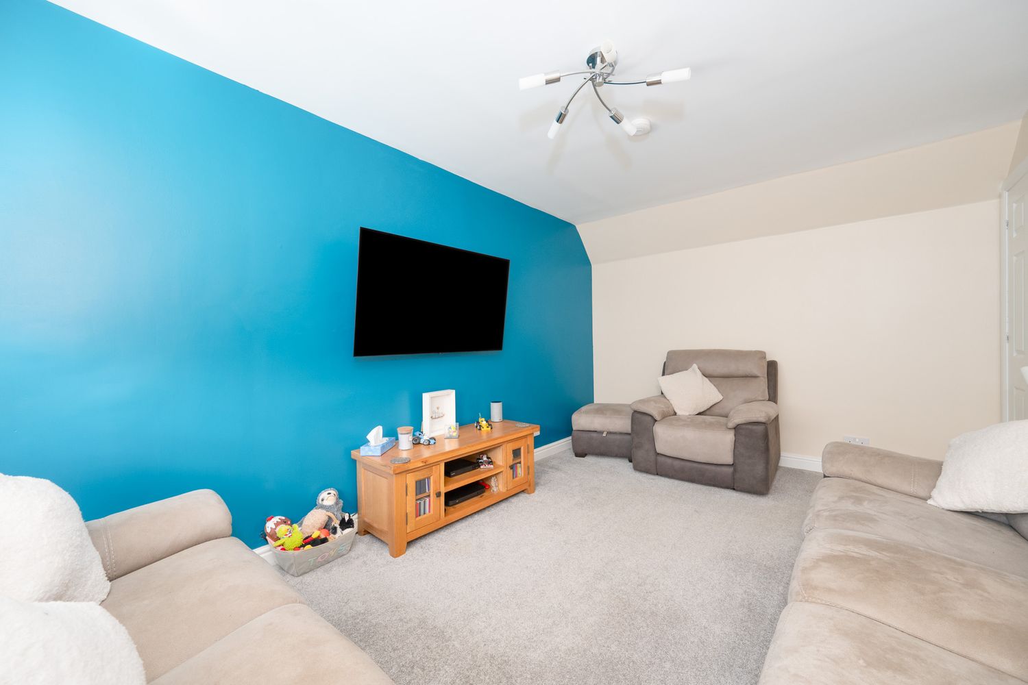 Modern living room with bright blue accent wall, wall-mounted TV, gray sofas and light carpeting.