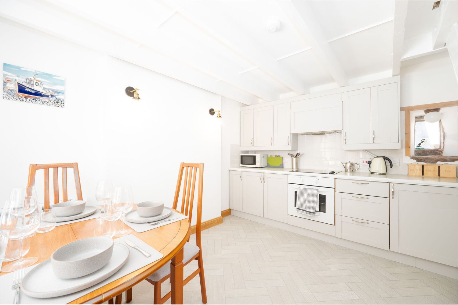 Modern white kitchen with wooden dining set and place settings in bright interior space.