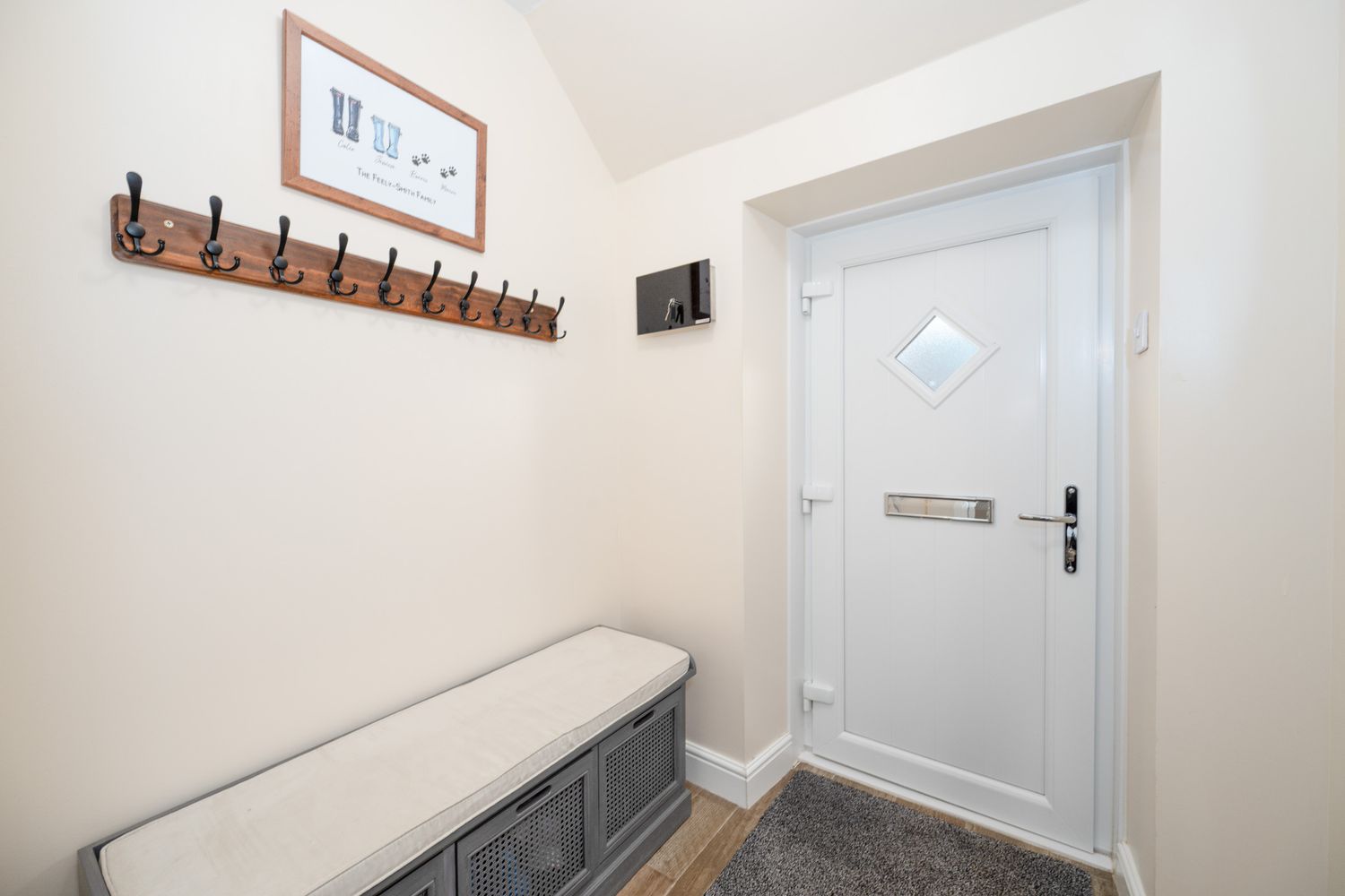 A white entryway with a wooden coat rack mounted on the wall and a gray storage bench against neutral walls.