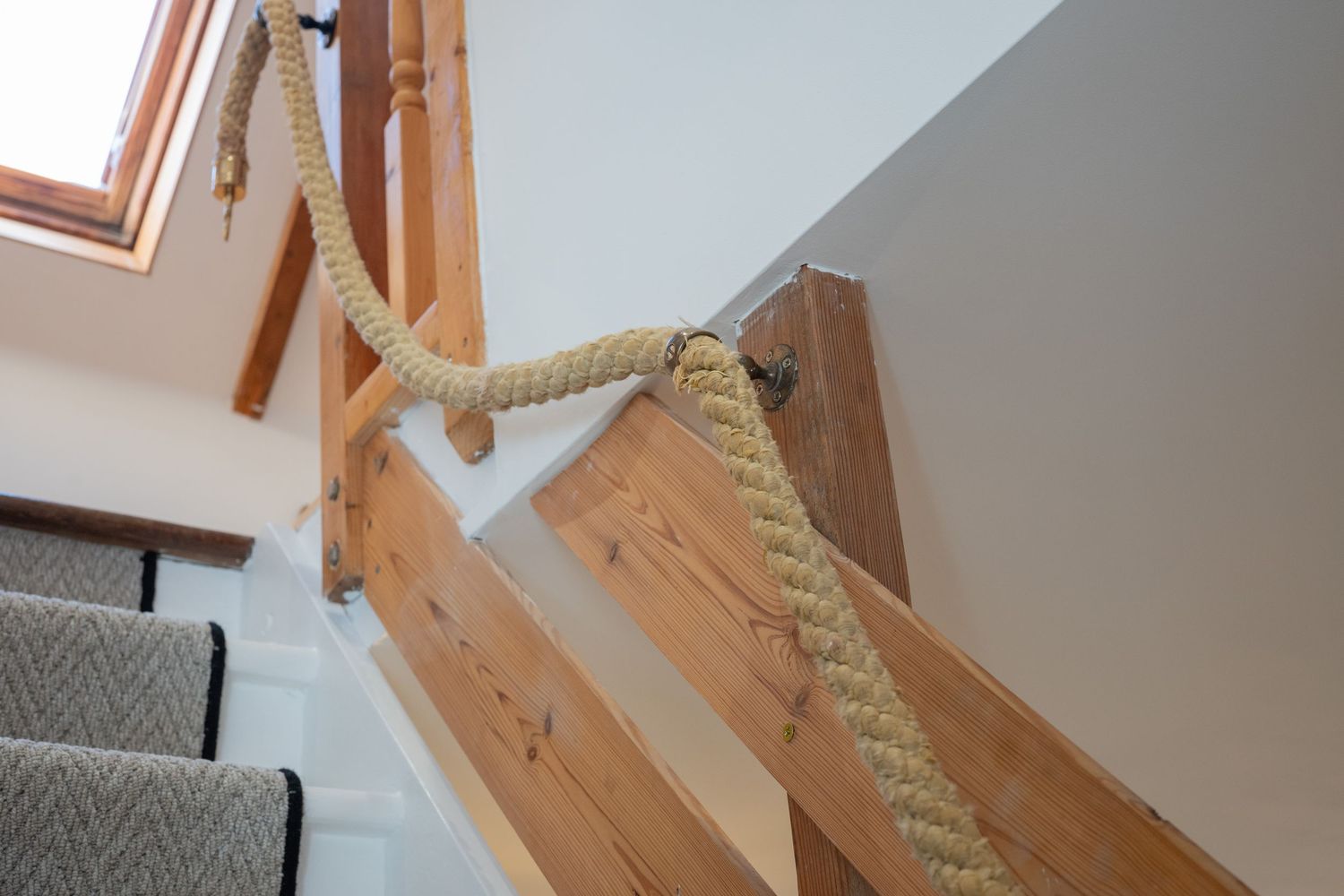 Nautical rope handrail installed along wooden stairs with gray carpet runner.