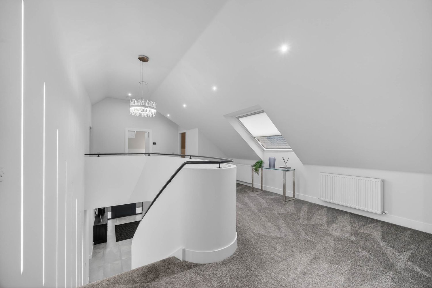 Modern white loft hallway with grey marble floors, skylight, and crystal chandelier features curved staircase railing.