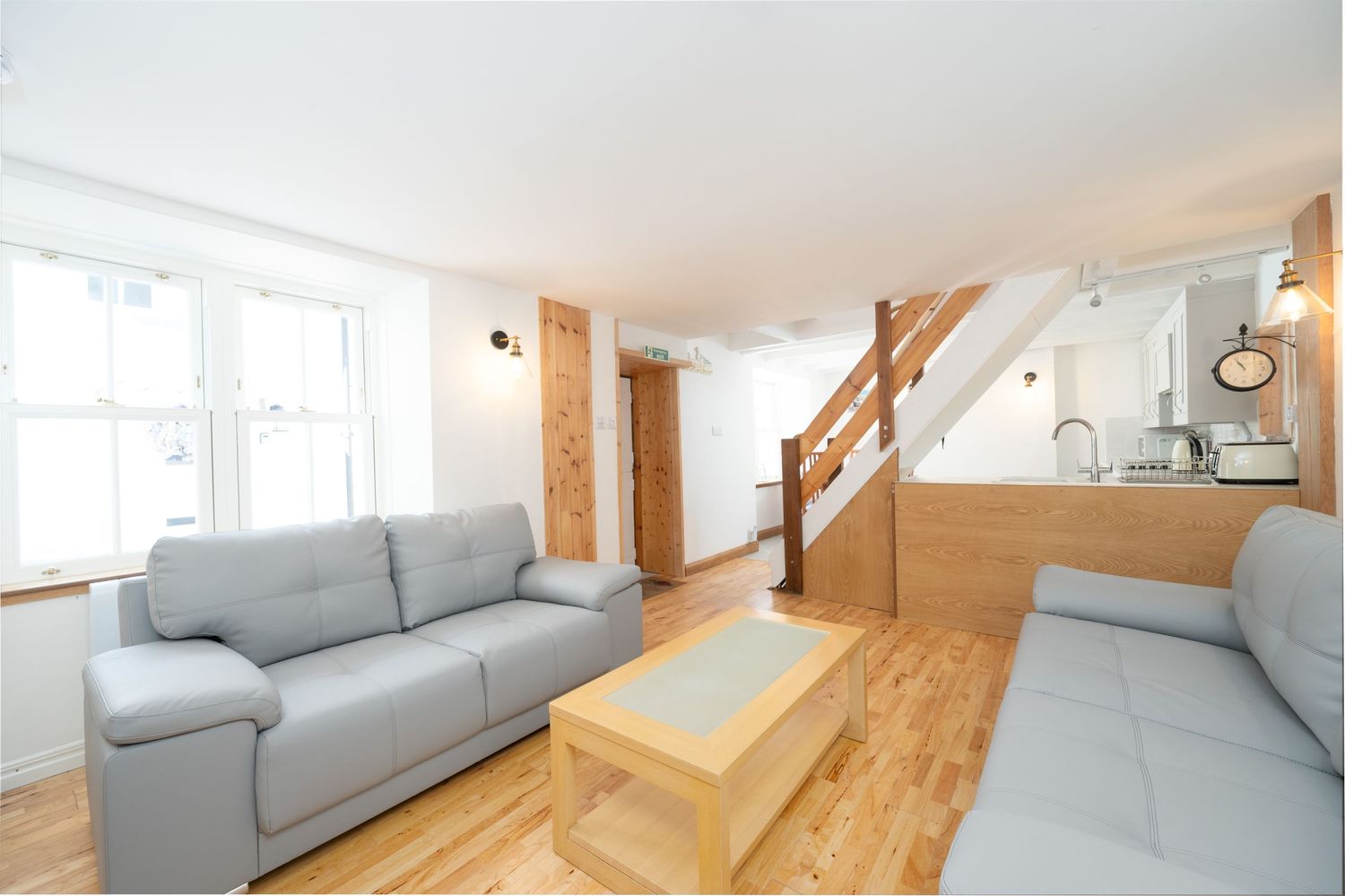 Modern living room interior with gray couches, wooden floors and stairs leading to an upper level.