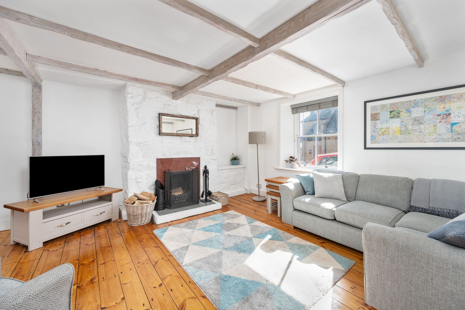 Modern living room with grey sofas, wooden floor, exposed beams, and brick fireplace features blue accents and natural light.