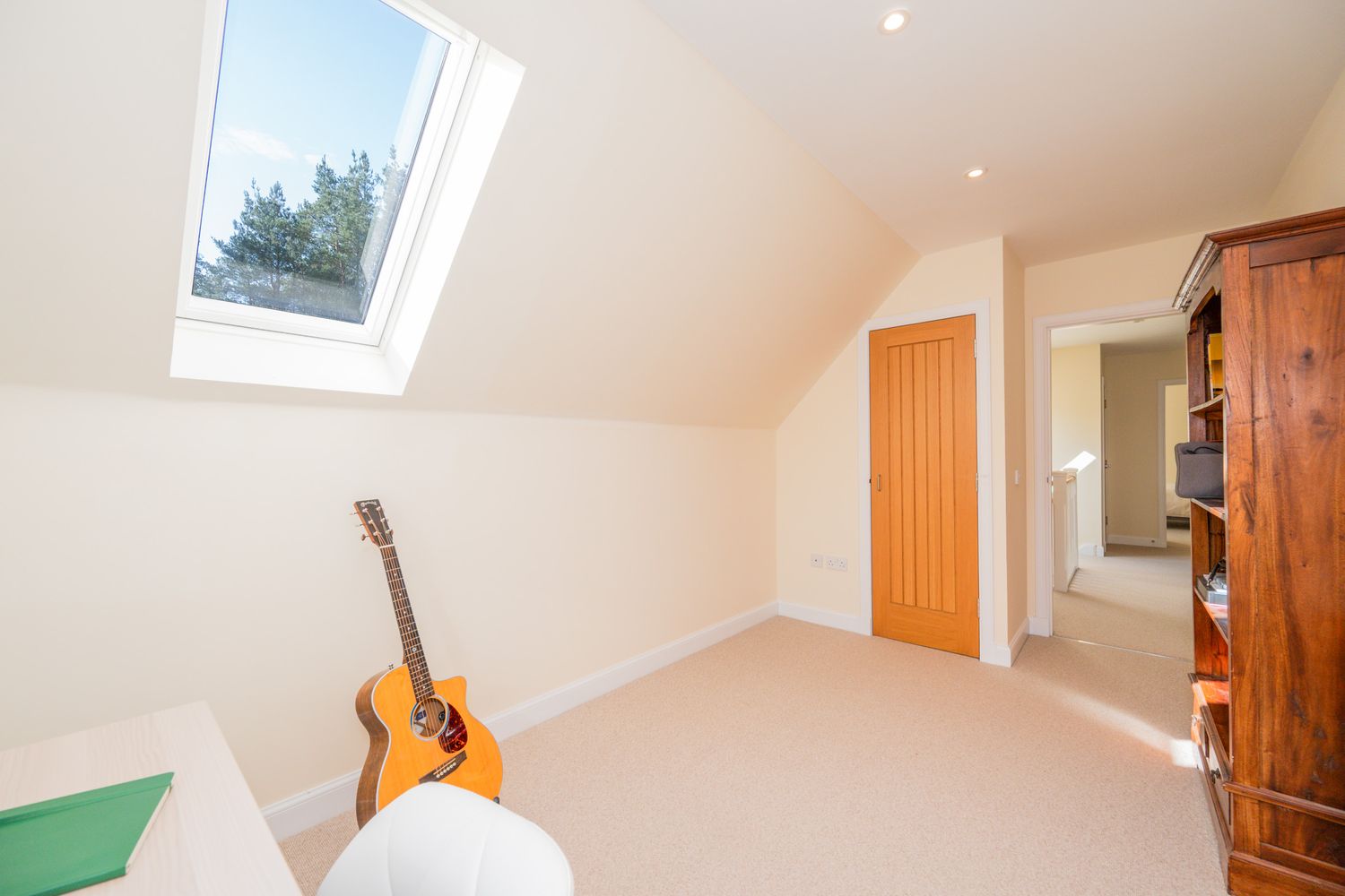Bright attic bedroom with skylight window, wooden door, carpet flooring and acoustic guitar leaning against white wall.