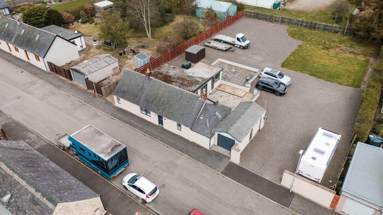 Aerial view of a small parking area with cars and buildings featuring gray rooftops in a residential neighborhood.