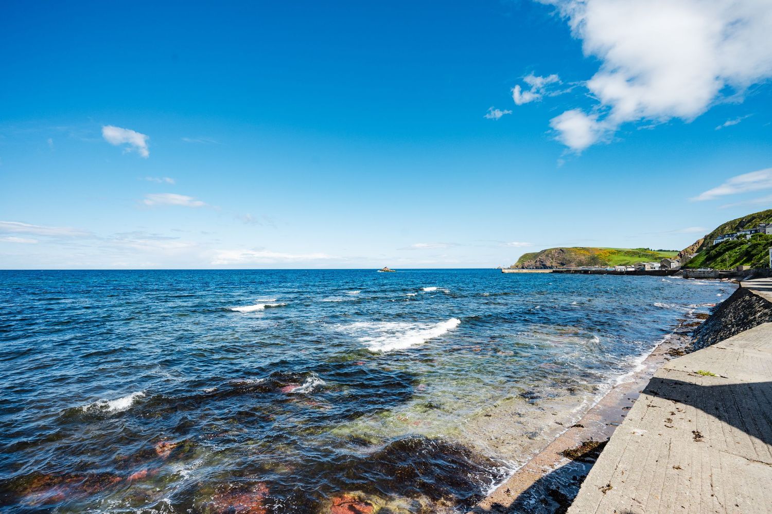 Scenic rocky coastline with blue ocean waters and green headlands under bright summer sky.