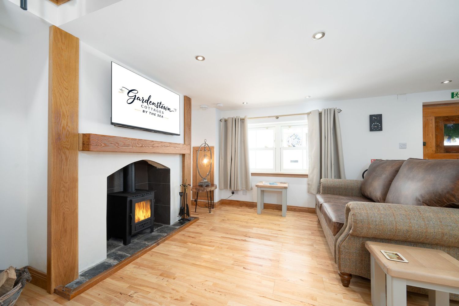 Modern living room interior with wooden flooring, gray fireplace insert, and comfortable brown sofa beneath mounted TV screen.