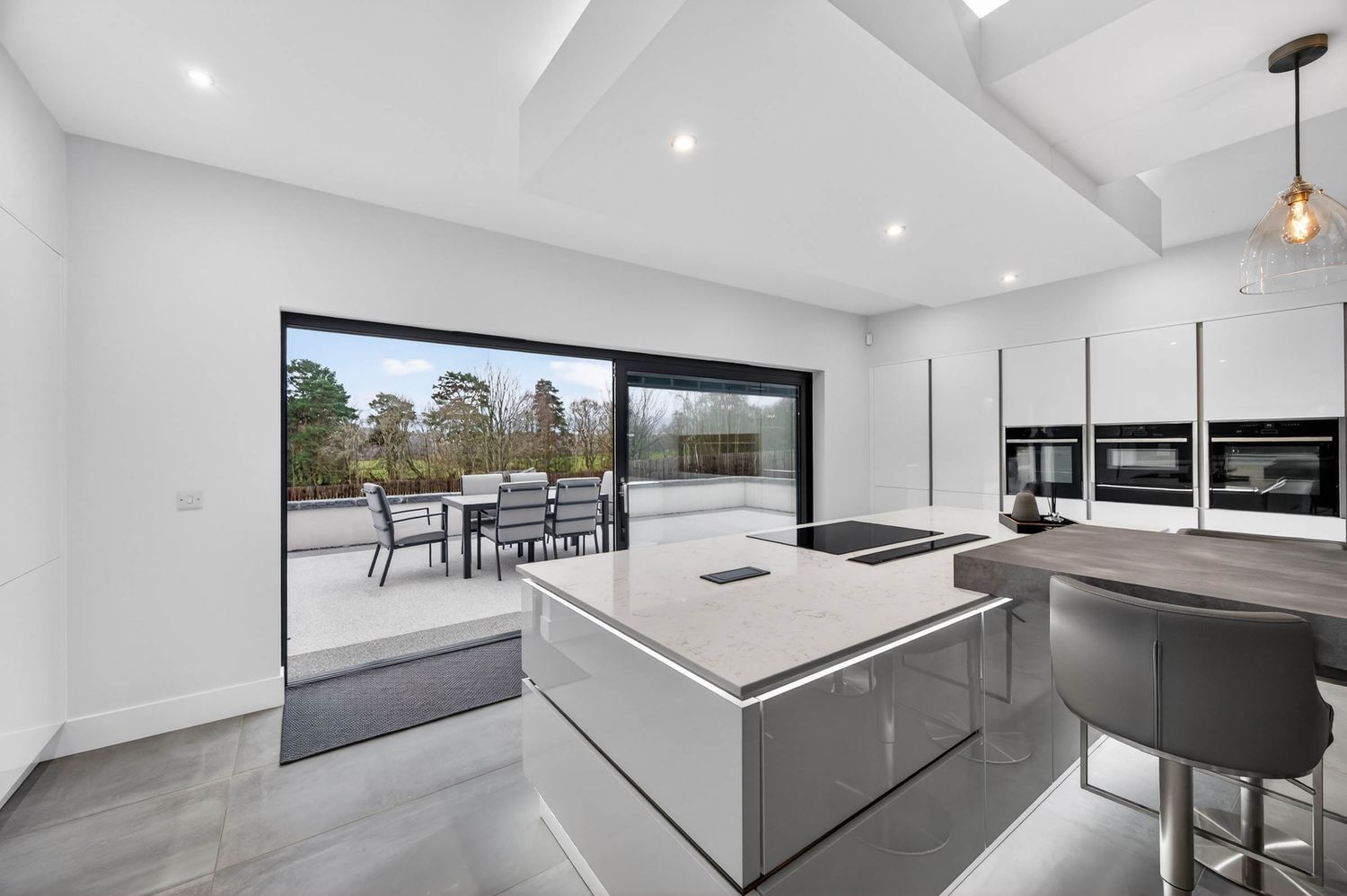 Modern white kitchen and living space with sleek minimalist design features pendant lighting and panoramic windows.