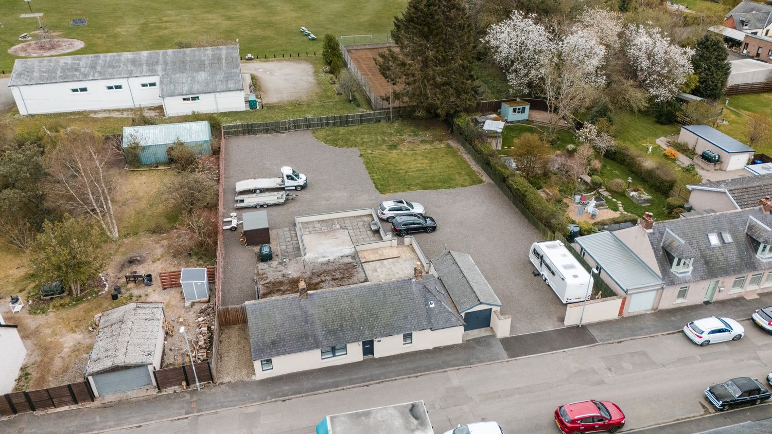 Aerial view of a commercial property with parking lot and buildings surrounded by trees and parked cars.