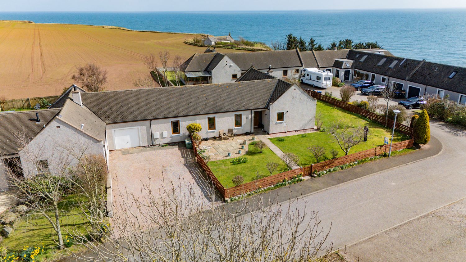 Aerial view of a white residential bungalow with garden near coastal cliffs and agricultural fields by the ocean.