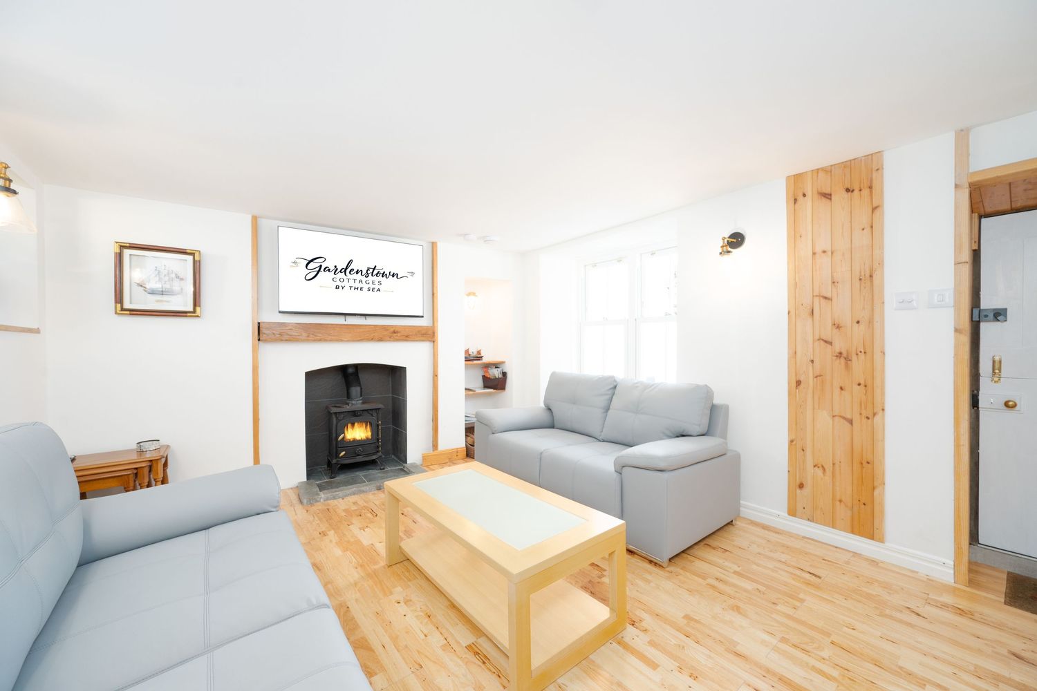 Modern living room with gray sofas, wooden coffee table, fireplace and pine wood flooring in bright natural light.