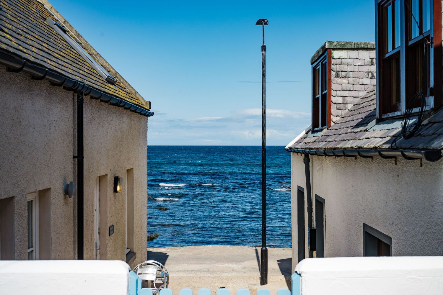 Seaside walkway between white buildings with blue ocean views and lamp posts.