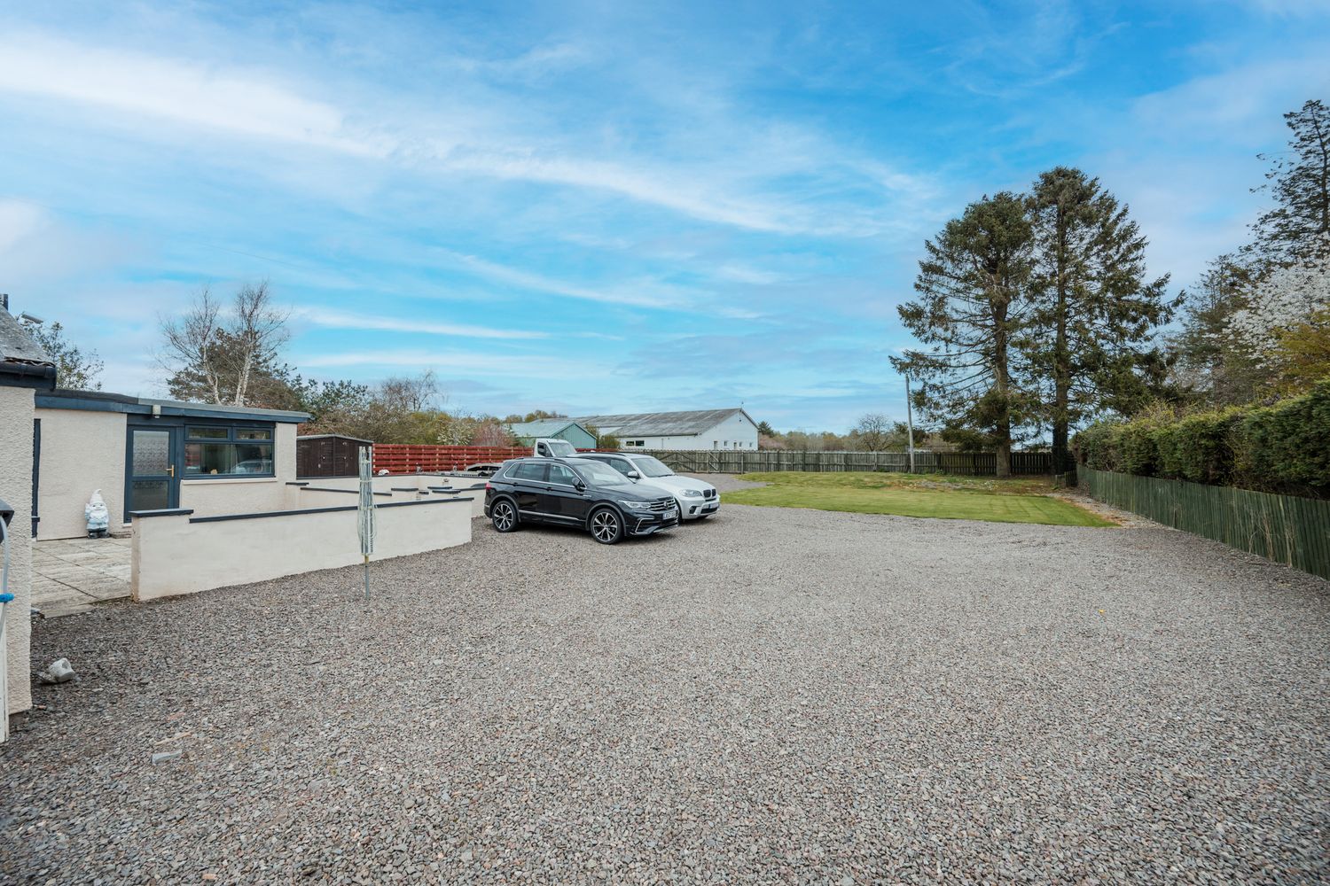 A gravel parking area with cars parked next to buildings under a blue sky with white clouds.