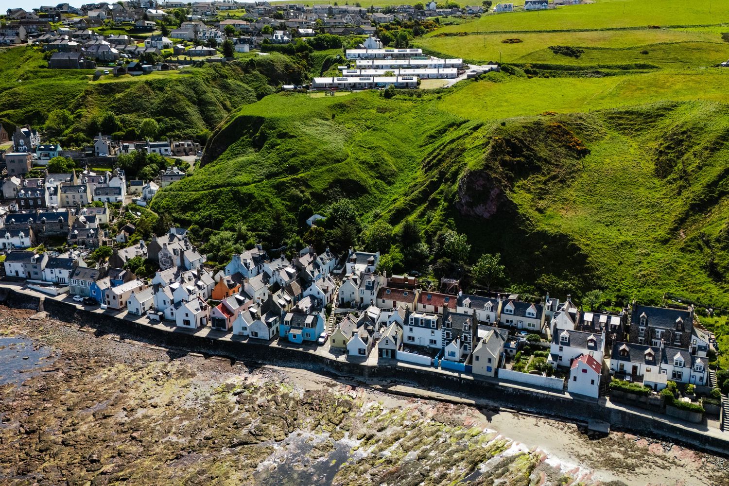 Scenic aerial view of white houses nestled along coastal cliffside with green hills in background.