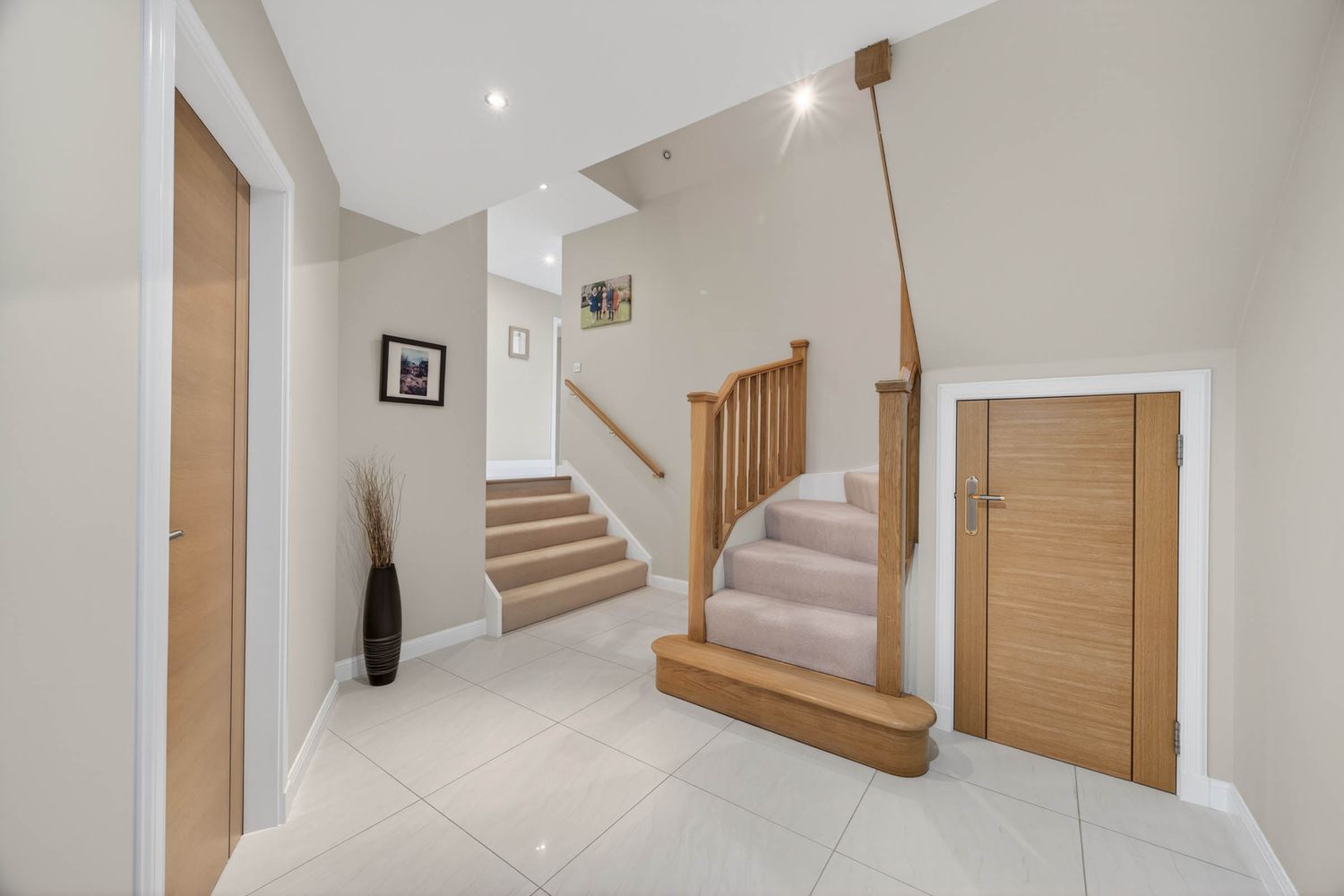 Bright hallway with wooden staircase, oak doors, and cream tiled flooring.
