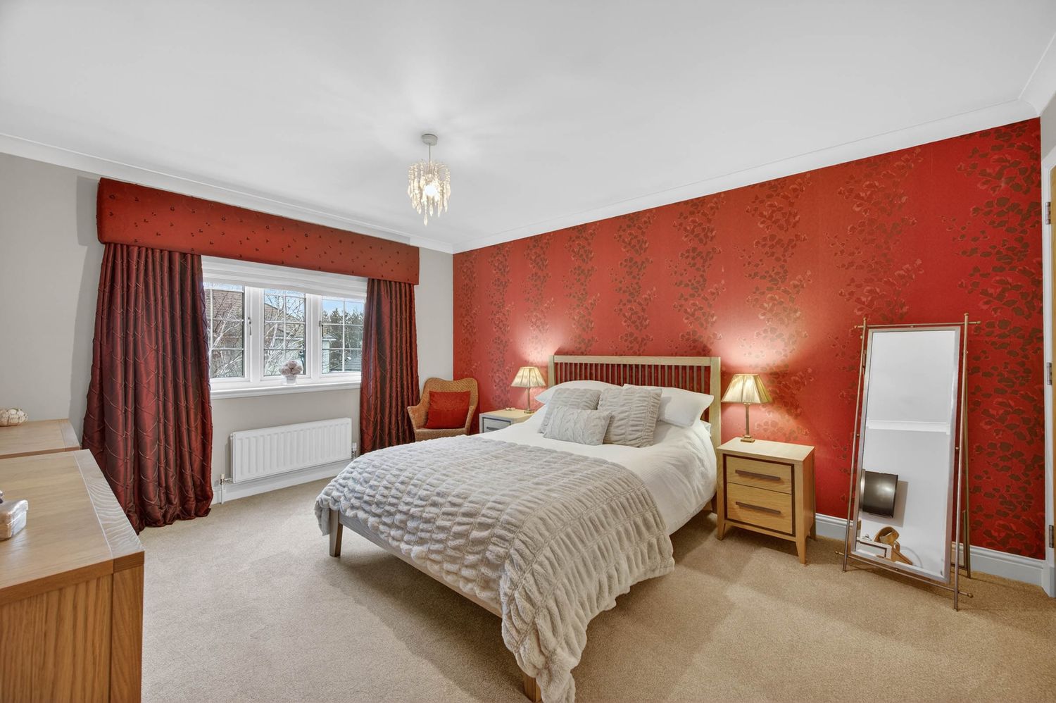 Bedroom with bold red accent wall, matching curtains, and quilted bedding in neutral tones.