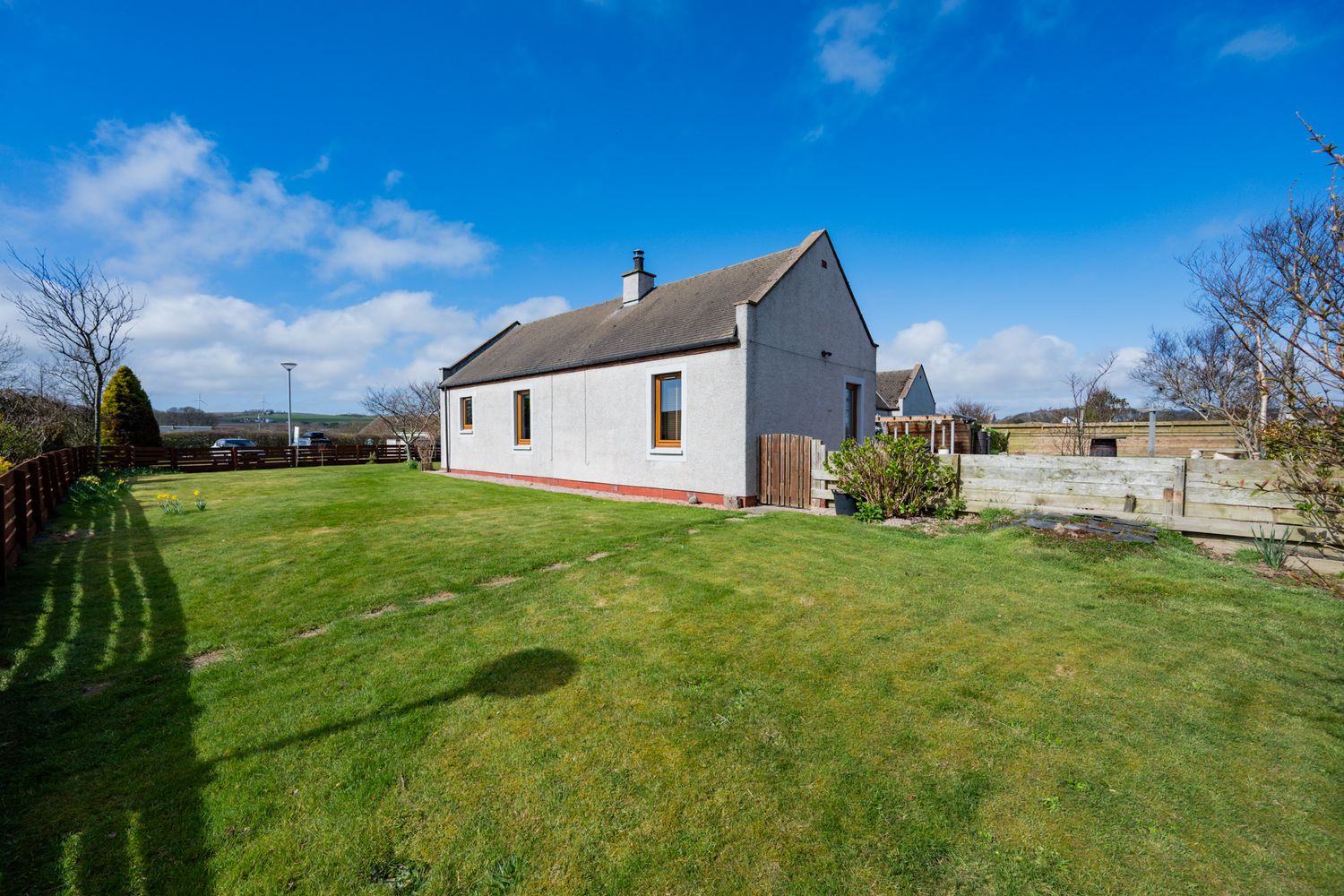 White cottage style house with large green lawn and blue sky in rural countryside setting.