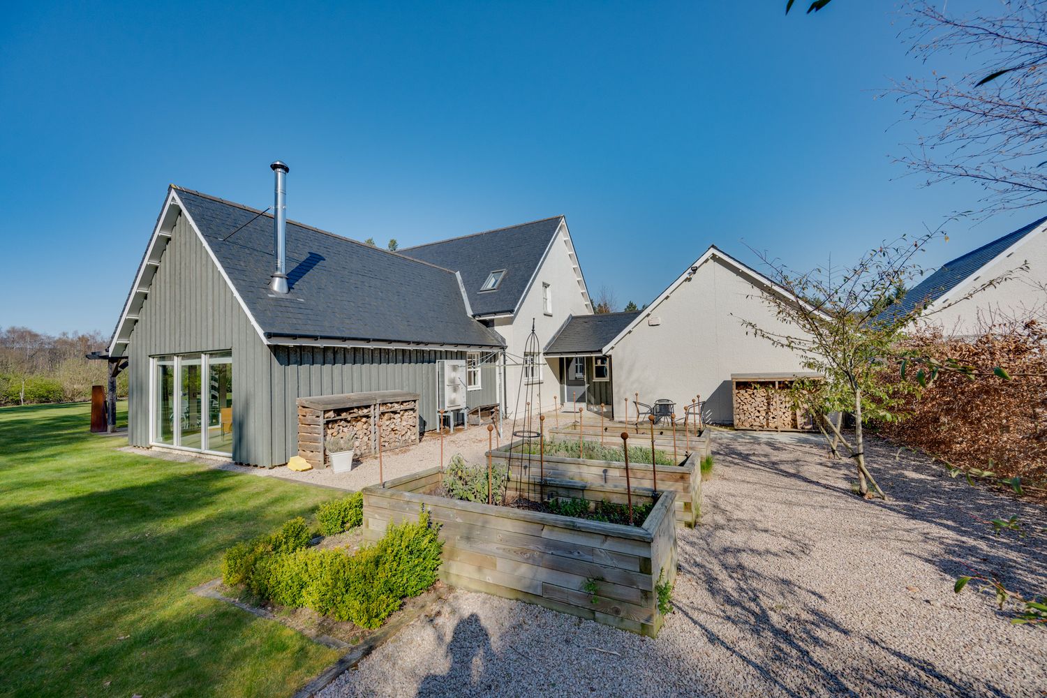 Modern farmhouse style home with gray exterior features multiple wings and landscaped garden on sunny day.