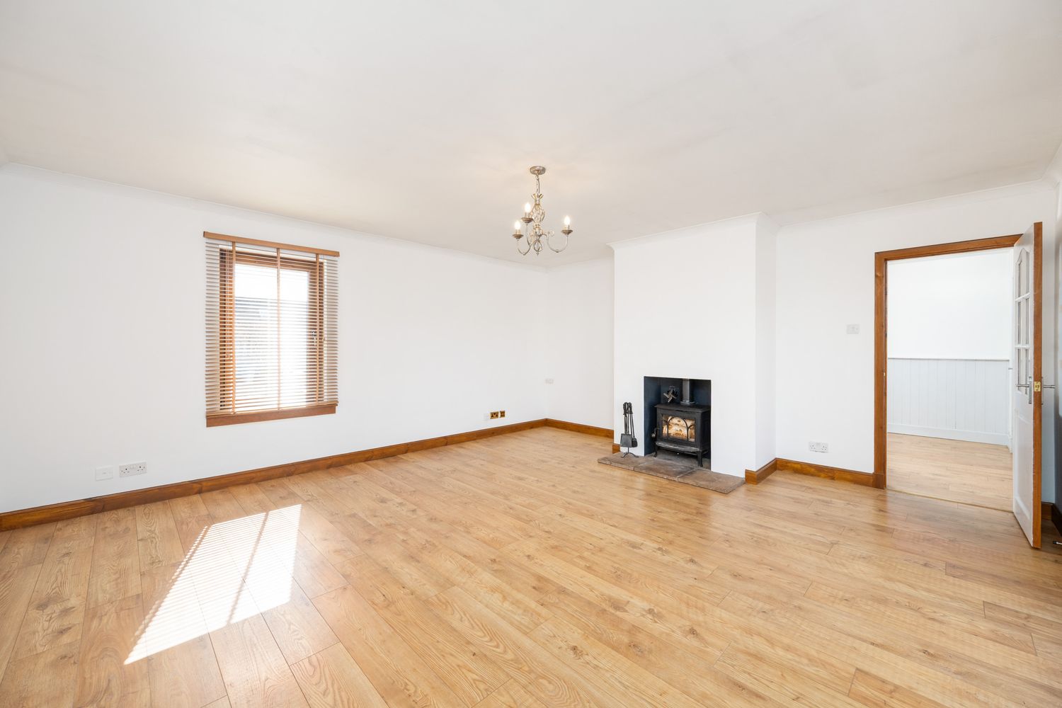 Empty living room interior with hardwood flooring, white walls, wooden framed windows and a corner fireplace.