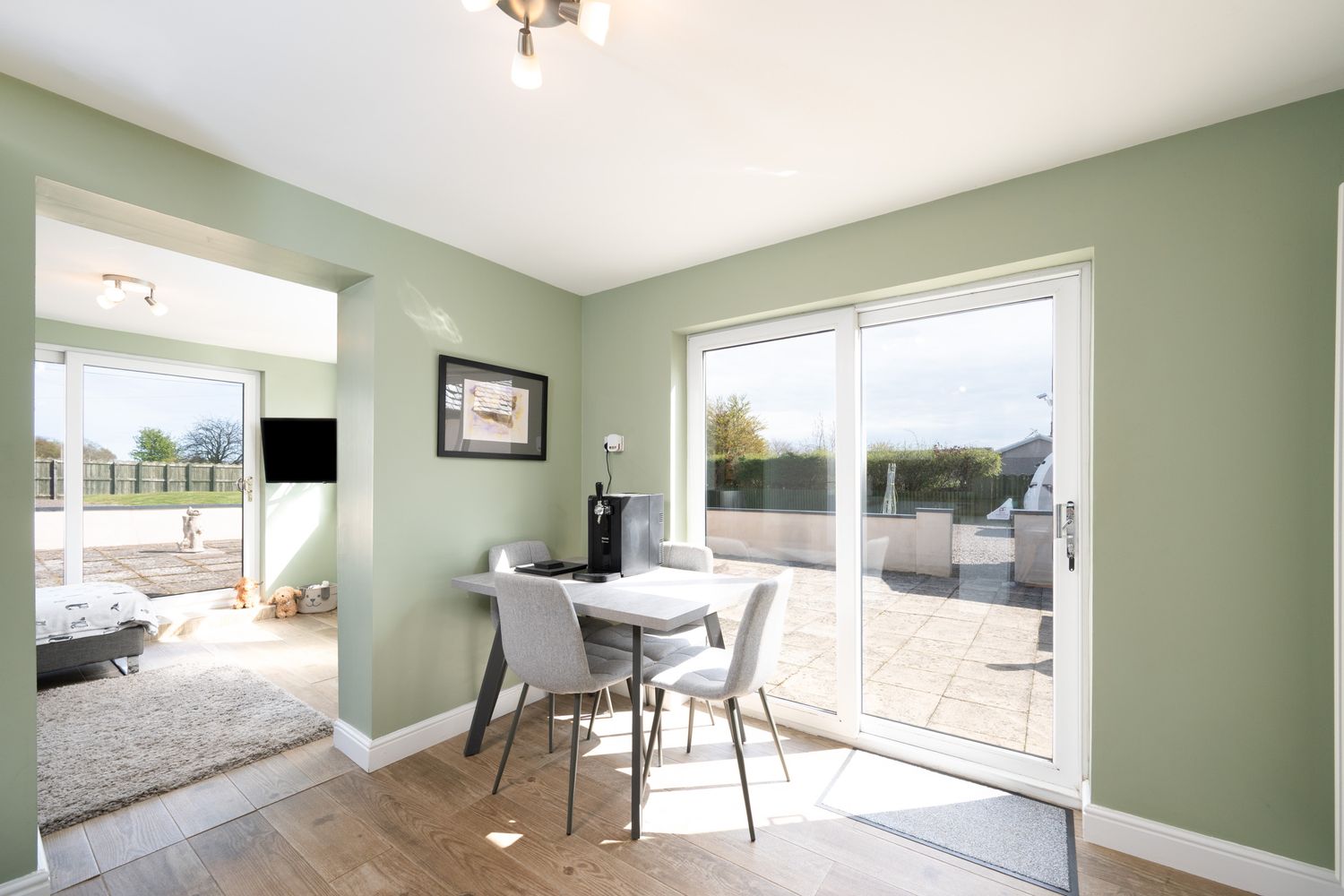 Modern dining nook with sage green walls, white table and chairs, and large sliding glass doors leading to patio.