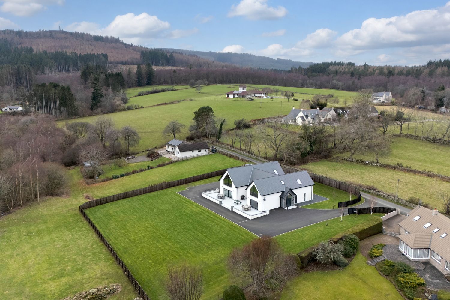 Panoramic aerial view of rolling green hills and scattered white houses in the Scottish countryside on a partly cloudy day.
