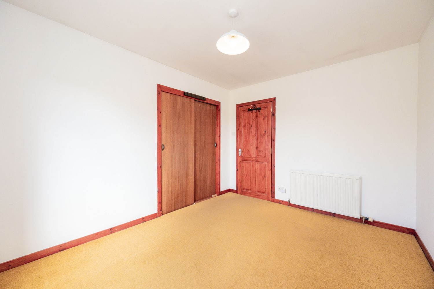 Vacant room with orange carpeting, white walls, and two wooden doors.