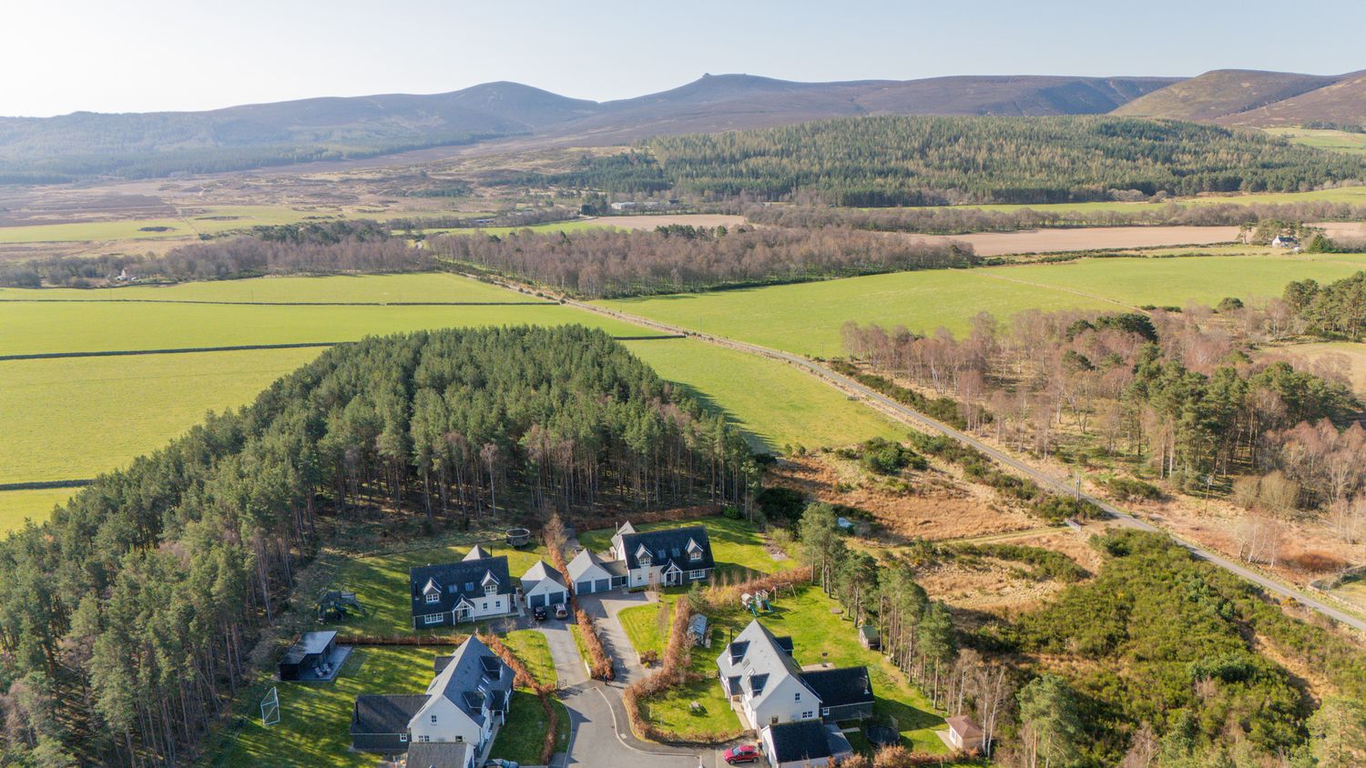 Aerial view of a secluded Scottish hamlet nestled among green fields and wooded hills in the rural countryside.