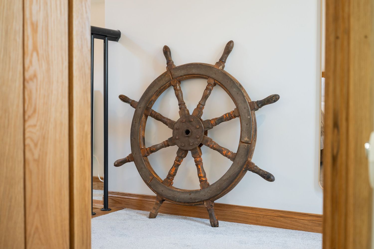 Vintage wooden ship wheel mounted on light wood paneled wall as nautical home decor.