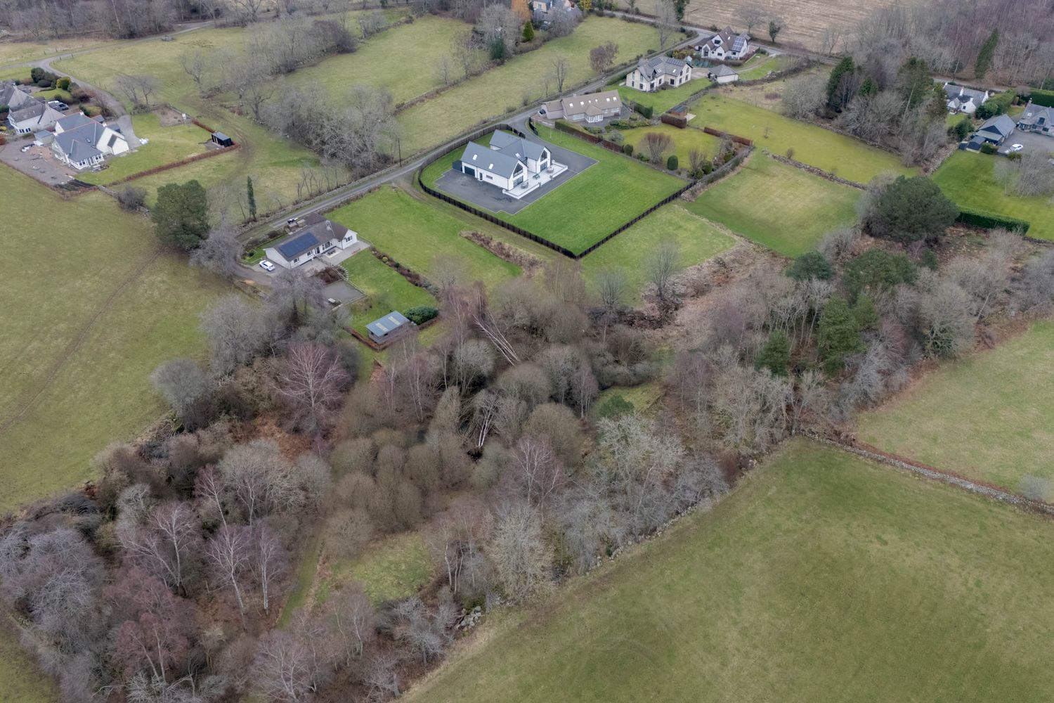Aerial view of rolling green hills with scattered houses and properties nestled among trees in a rural landscape.