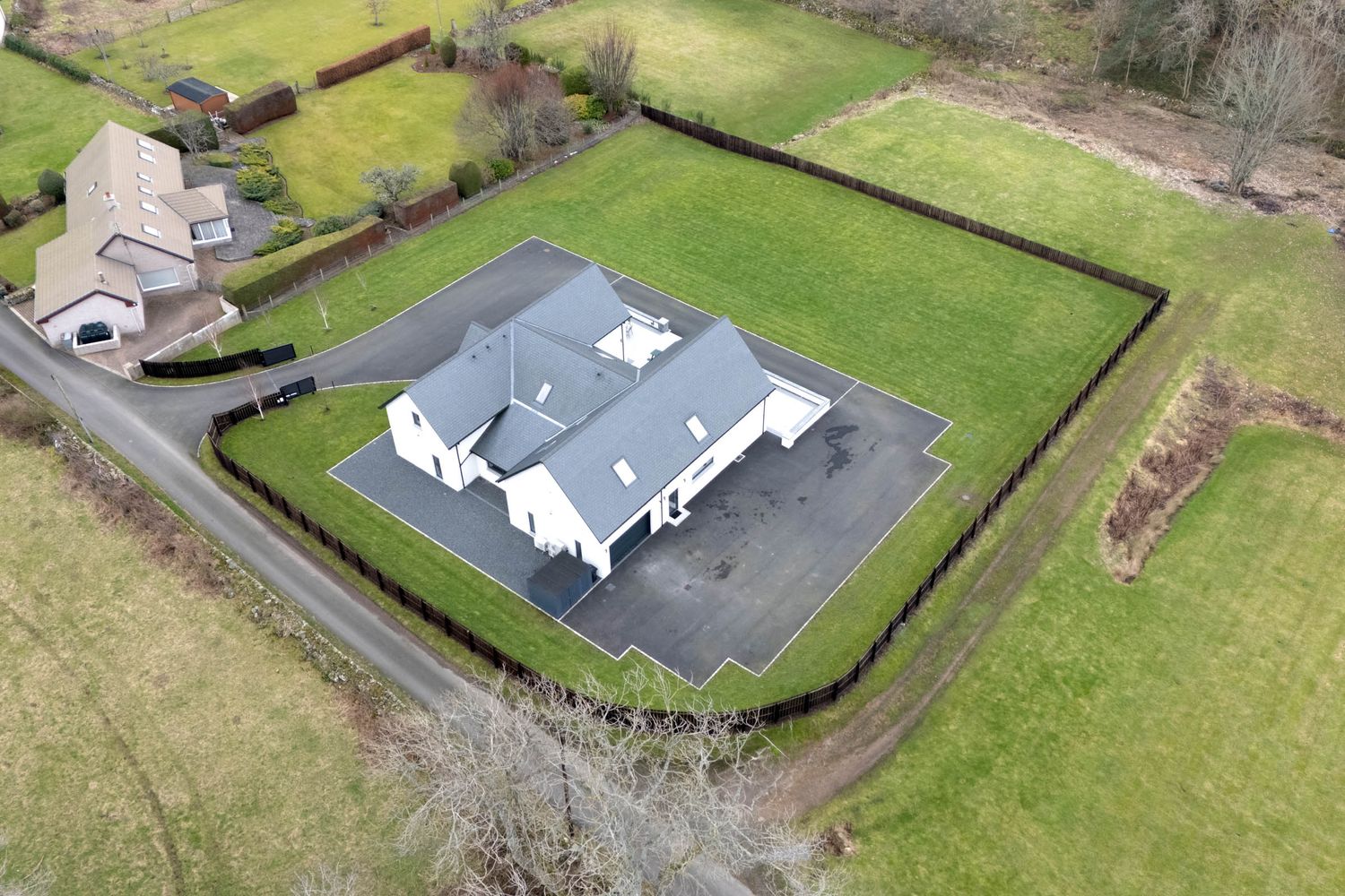 Aerial view of a modern house with grey roof and white walls surrounded by green lawns and hedges.