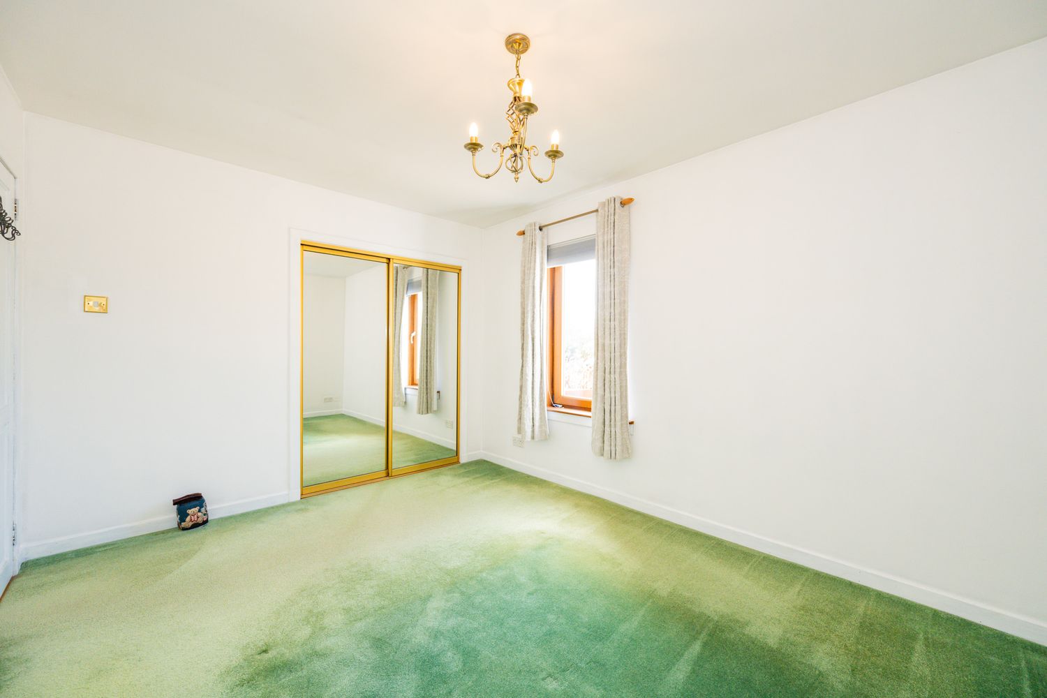 Spacious room with mint green carpeting, white walls, and a brass chandelier.