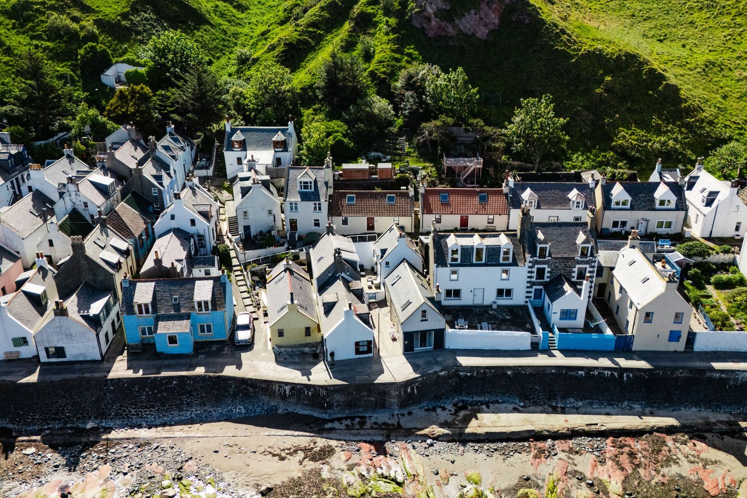 Aerial view of white coastal houses lined up along rocky shoreline in Scottish fishing village.