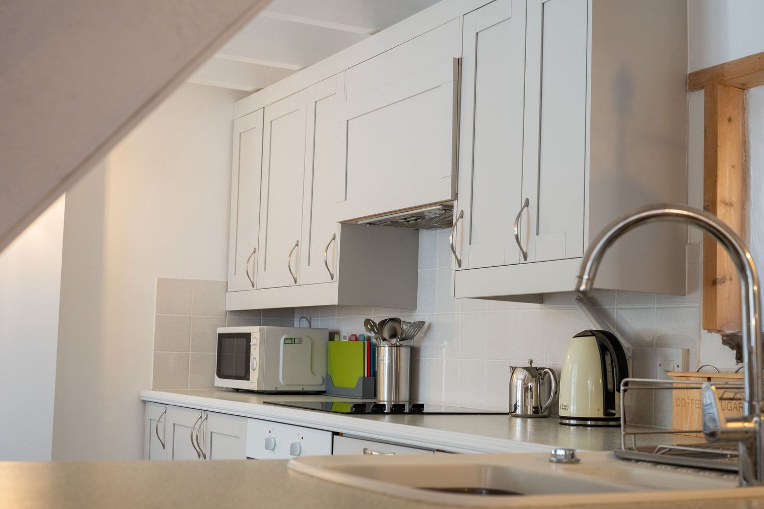 Modern white kitchen with under-cabinet lighting, built-in appliances and stainless steel sink.