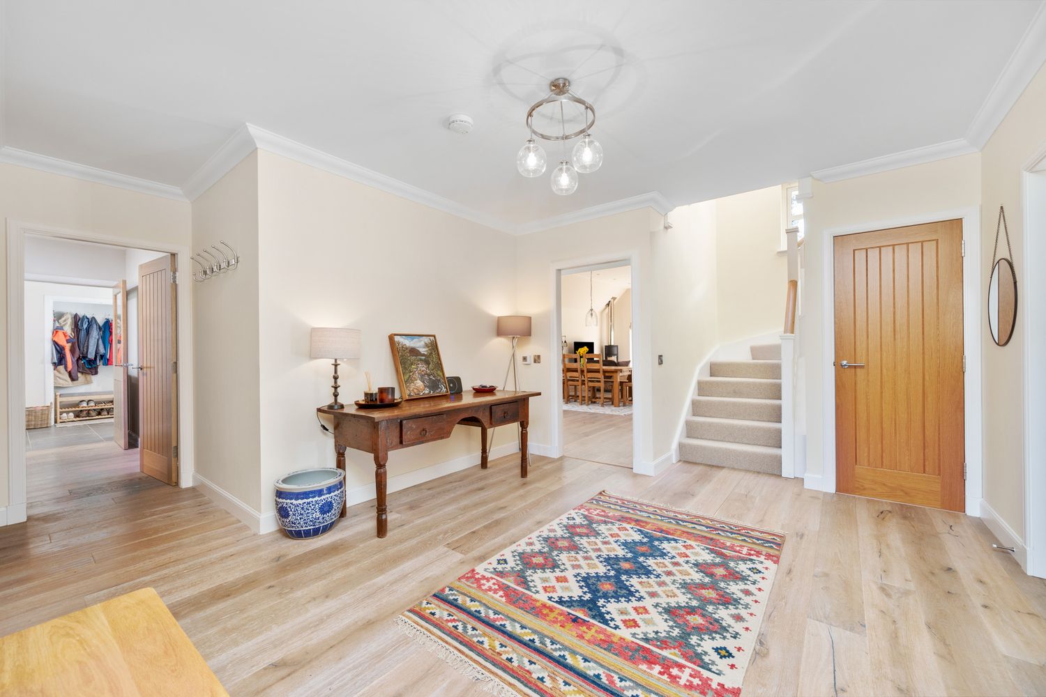 Bright entryway featuring hardwood floors, a console table, and colorful patterned rug leading to stairs and hallway.