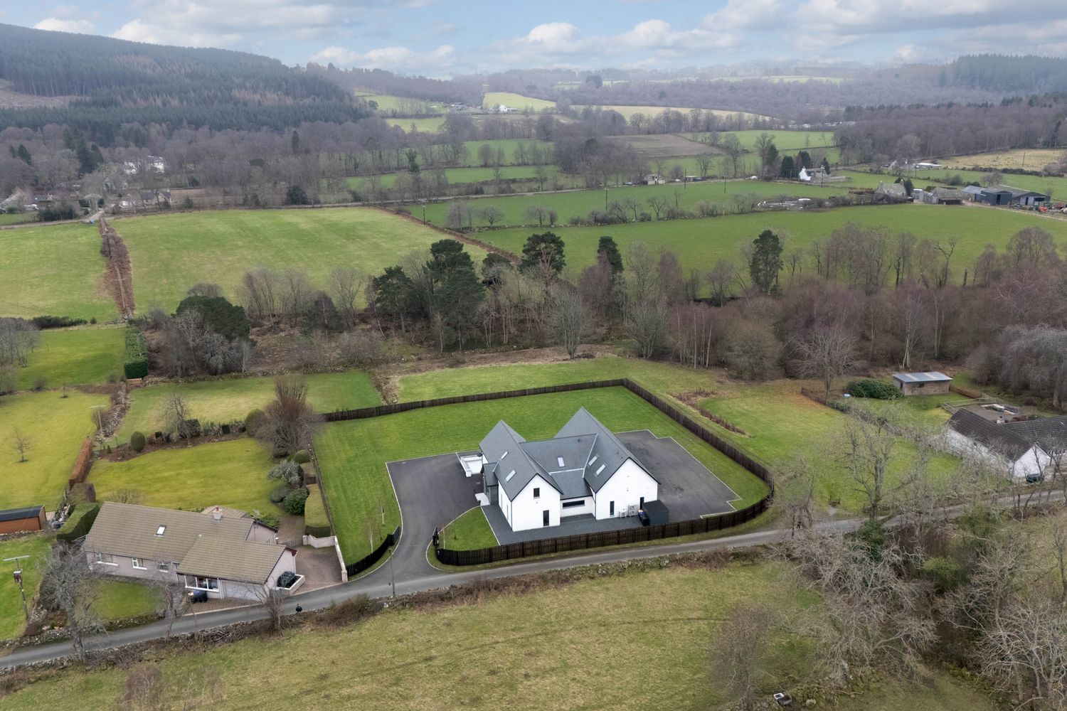 Panoramic aerial view of rolling green hills with scattered houses and trees in a rural countryside landscape.